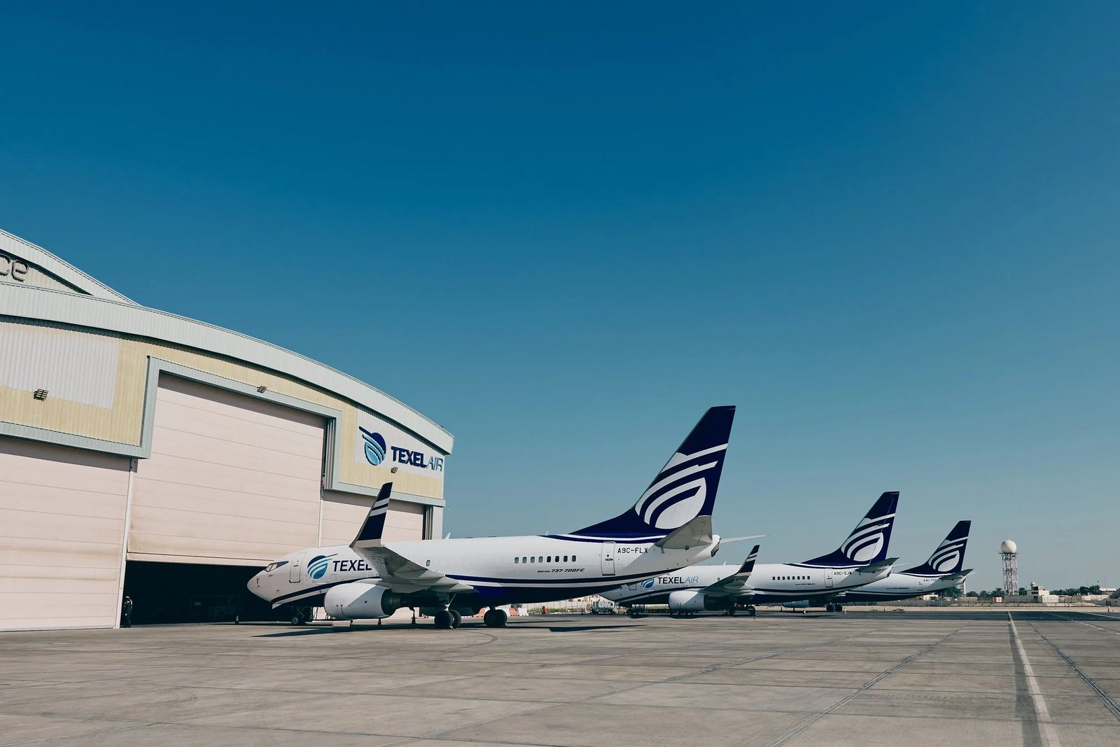 A line of Texel Air 737 aircraft parked beside a hangar under a blue sky.